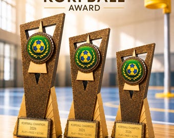 May include: Three bronze-colored trophies of varying heights featuring a central circular emblem with a blue and yellow ball graphic. Each trophy base has a plaque reading KORFBALL CHAMPION 2026 PLAY PASS SCORE in black text on a gold background.