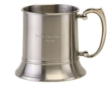 May include: A silver stainless steel beer stein with a handle. The stein has a smooth, polished finish and a wide base. The text "YOUR ENGRAVING HERE" is engraved on the front of the stein.