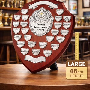May include: A large, shield-shaped achievement award with a dark wood finish. It features silver plaques for various achievements and the text "Overall Achievement Award." The award is 46cm in height.