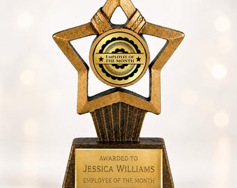 May include: A gold-toned star-shaped trophy featuring a central circular emblem with the text "EMPLOYEE OF THE MONTH" and two stars. The base includes a rectangular gold plaque engraved with "AWARDED TO JESSICA WILLIAMS EMPLOYEE OF THE MONTH."