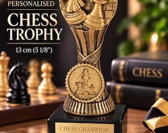 May include: A gold-colored chess trophy measuring 5 1/8 inches tall, featuring a knight and king piece on a circular checkered base. The trophy sits on a black square plinth with a gold plaque engraved with the text CHESS CHAMPION 2026.