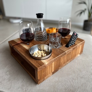 Könnte beinhalten: Ein Holztablett mit Fächern für Gläser, eine Schüssel mit Nüssen und eine Fernbedienung. Das Tablett ist aus hellbraunem Holz gefertigt und hat eine natürliche Oberfläche.