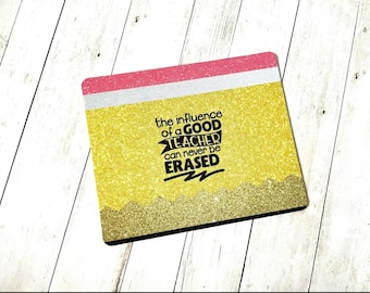 May include: A yellow and pink glitter mouse pad with the text "The influence of a good teacher can never be erased" in black.