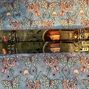 May include: Two packs of HEM incense sticks with the text "Black Aglaia Agra Magic" and "Incense Sticks" printed on the front. The packaging is black with gold lettering and a design of a building with a tower.