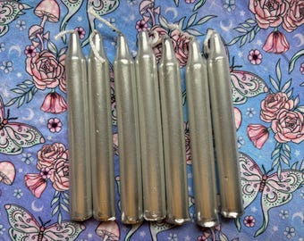 May include: A set of seven silver candle sticks, arranged in a row on a floral patterned surface. The candles are all the same size and shape, and they are made of a smooth, shiny material.