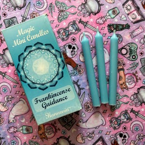 May include: A box of blue frankincense guidance mini candles with the text "Magic Mini Candles" and "Frankincense Guidance" on the front. The box is on a pink and white background with a variety of illustrations.