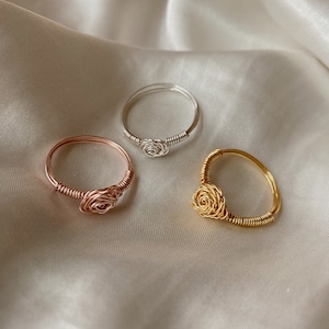 May include: Three wire wrapped rings with rose designs. The rings are silver, rose gold, and gold.