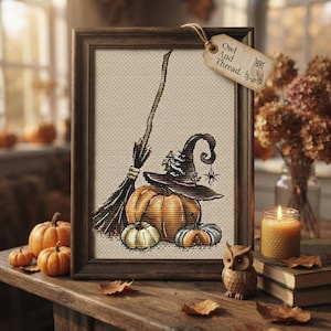 May include: A framed cross-stitch embroidery featuring a broomstick, a witch hat, and three pumpkins on a beige fabric background. A small paper tag attached to the top right corner of the dark wood frame reads Owl And Thread with an owl icon.