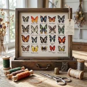Op de afbeelding: Een in hout ingelijst borduurwerk met twintig kleurrijke vlinderillustraties met wetenschappelijke namen, vergezeld van een label met Owl and Thread Collection, houten garenklosjes, een metalen vingerhoed en een schaar.