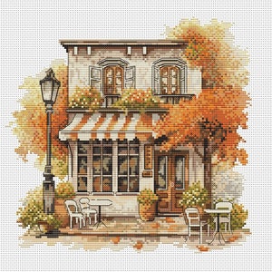 Könnte beinhalten: Eine Kreuzstich-Illustration eines charmanten Cafés mit einem gestreiften Vordach, umgeben von Herbstlaub. Das Café hat ein großes Fenster, eine Tür und zwei Tische mit Stühlen im Freien. Eine Straßenlaterne steht neben dem Café.