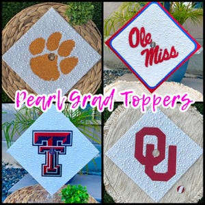 Può includere: Quattro cappelli di laurea con abbellimenti di perle e loghi universitari. I cappelli presentano un'impronta di zampa, le parole "Ole Miss", il logo Texas Tech e il logo Oklahoma Sooners. Il testo "Pearl Grad Toppers" è anch'esso visibile.