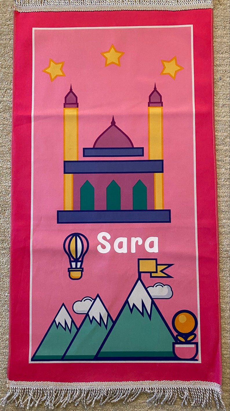 May include: Pink prayer rug with a mosque, stars, mountains, a hot air balloon, and the name "Sara" printed on it.