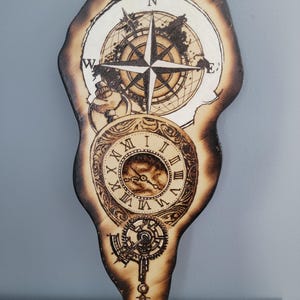 May include: Wooden wall art featuring a compass rose, world map, and clock design. The artwork is intricately burned into the wood, showcasing a vintage, steampunk aesthetic. The piece includes Roman numerals and gear details.