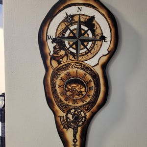 May include: A wooden wall art piece featuring a compass rose and a clock design. The artwork is in shades of brown and tan, with intricate details and a vintage aesthetic. The compass rose is at the top, and the clock is below.
