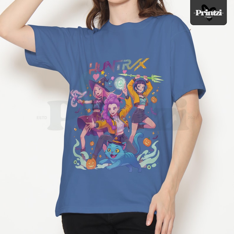 May include: Blue t-shirt featuring a colorful graphic of three anime-style characters with magical elements, a blue cat, and pumpkins. The word "HUNTR/K" is printed above the characters in pink and green.