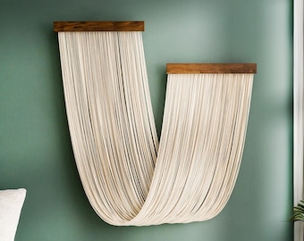 May include: A wall hanging made of white string, shaped like a U, with a wooden top and bottom. The wall hanging is against a green wall.