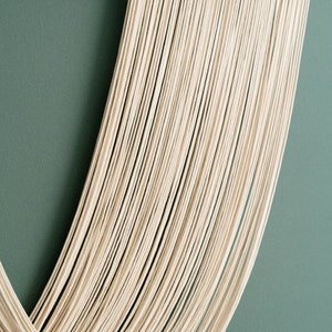 May include: A white macrame wall hanging with a wooden frame. The macrame is made of many strands of yarn that are woven together to create a unique design.