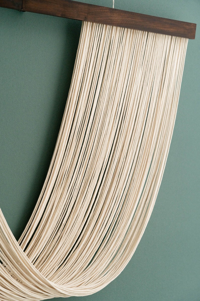 May include: A white macrame wall hanging with a wooden frame. The macrame is made of many strands of yarn that are woven together to create a unique design.
