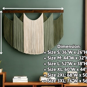 May include: A macrame wall hanging with a wooden bar. The design features a central cream-colored section flanked by olive green sections. Dimensions are provided, with the smallest size being 36"W x 26"H.
