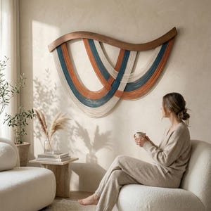 May include: A large wall hanging with a wooden frame and cascading strands in orange, teal, and cream colors. The artwork is mounted on a neutral-toned wall. The piece adds a modern, artistic touch to the room.