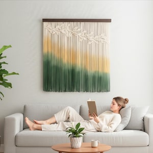 May include: A large, rectangular macrame wall hanging with a wooden top bar. The design features a gradient of colors, transitioning from cream to yellow and then to green. Decorative cream-colored leaf patterns are at the top.