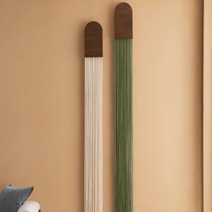 May include: Two wall hangings with wooden tops and long strands of yarn hanging down. The yarn on the left is white and the yarn on the right is green.