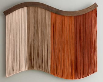 May include: A wall hanging with a wooden, curved top and vertical strands in shades of beige, brown, and orange. The textured strands create a flowing, wave-like design. This decorative piece adds a touch of warmth and texture to any space.