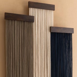 Puede incluir: Tres tapices de pared hechos de cuerda con marcos de madera. El tapiz de la izquierda está hecho de cuerda marrón, el tapiz del medio está hecho de cuerda blanca y el tapiz de la derecha está hecho de cuerda negra.