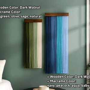 May include: Two macrame wall hangings with dark walnut wooden tops. One features dark green, olive, sage, and natural colored macrame. The other displays navy, peacock, aqua, and baby blue macrame. Both are displayed against a green wall.