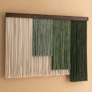 Pode incluir: Uma tapeçaria de parede moderna com uma moldura de madeira escura e fios verticais em tons de verde e creme. O design texturizado cria um efeito artístico em camadas, adequado para decoração de casa.
