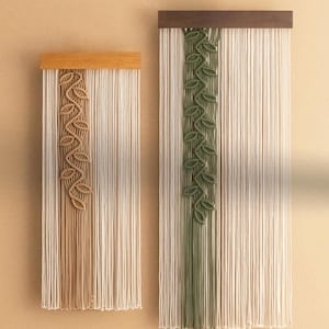 May include: Two macrame wall hangings with wooden frames. The left one has a tan leaf design and the right one has a green leaf design.