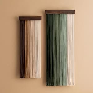 Op de afbeelding: Twee wandhangers gemaakt van garen, elk met een houten bovenbalk. De linker hanger heeft bruin, beige en wit garen. De rechter hanger heeft groen en wit garen.