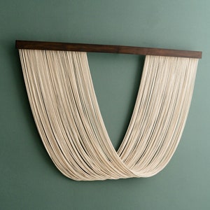 May include: A wall hanging made of white string, woven into a V-shape, with a dark wood frame.