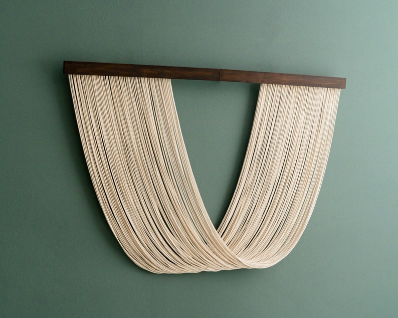 May include: A wall hanging made of white string, woven into a V-shape, with a dark wood frame.