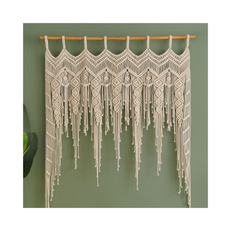 May include: A beige macrame wall hanging with a wooden dowel rod at the top. The hanging features a geometric pattern with fringe details.