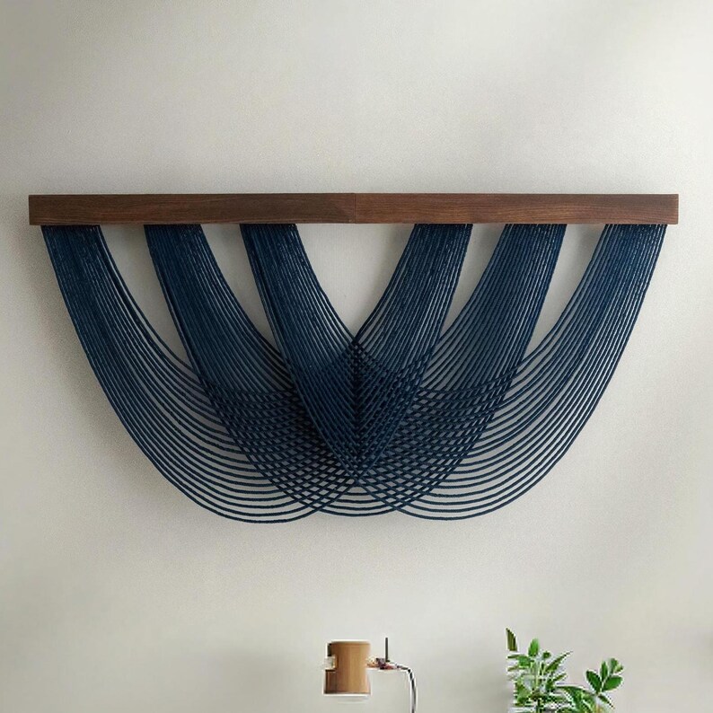 May include: A modern wall art piece featuring navy blue strings suspended from a dark brown wooden beam. The strings are arranged in a curved, layered pattern, creating a unique and artistic design. This decorative item adds a touch of contemporary style to any interior space.