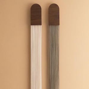 Puede incluir: Dos tapices de pared con tapas de madera y largos hilos de hilo que cuelgan. El hilo de la izquierda es blanco y el hilo de la derecha es marrón.