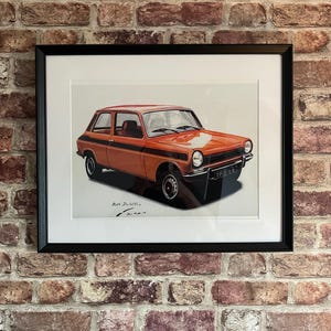Può includere: Una stampa incorniciata di un'auto vintage arancione con dettagli neri. L'auto è una hatchback con una striscia nera che corre lungo il lato. La stampa è firmata "Marc Delettrez" in basso a destra.
