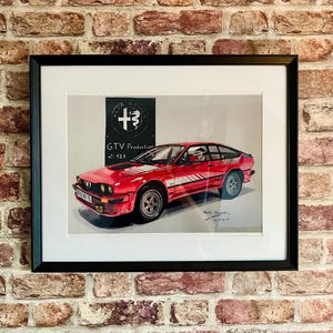 Puede incluir: Una impresión enmarcada de un coche rojo Alfa Romeo GTV con una franja blanca. El coche está sobre un fondo blanco con el texto "Alfa Romeo GTV Production No. 123" encima.