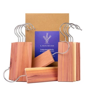 Könnte beinhalten: Ein Satz Zedernholz-Kleiderbügel mit Lavendel-Duft. Die Bügel sind aus natürlichem Zedernholz gefertigt und sollen dazu beitragen, dass Kleidung frisch und mottenfrei bleibt. Die Bügel sind in einer Schachtel mit einem Etikett verpackt, auf dem "LAVENDAS Zedernhol-blöcke aus hochwertigen Zedernholz" steht.