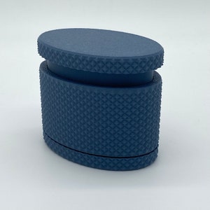Puede incluir: Un contenedor ovalado de color azul oscuro con un patrón texturizado. El contenedor tiene una tapa que se ajusta perfectamente en la parte superior.