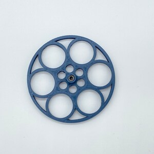 Könnte beinhalten: Eine blaue Filmrolle aus Kunststoff mit sechs kreisförmigen Öffnungen. Die Rolle hat ein kleines Metall-Mittelstück.