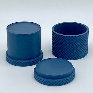 Könnte beinhalten: Dreiteiliges Set aus marineblauen Behältern. Einer ist ein Zylinder mit flacher Oberseite und strukturierter Basis. Ein weiterer ist ein Hohlzylinder mit Rautenmuster. Der dritte ist eine flache Scheibe mit strukturierter Basis.