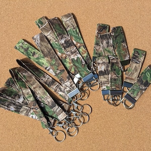 May include: A group of camouflage patterned keychains with silver key rings. The keychains are made of fabric and have a variety of different patterns.
