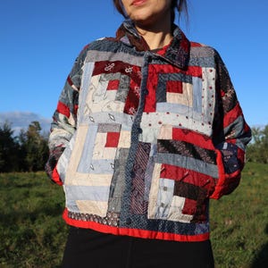 May include: A quilted jacket featuring a patchwork design of various fabrics in shades of red, blue, grey, and black. The garment has a collared neckline, a front button closure, and two front pockets, constructed with a visible stitched pattern.