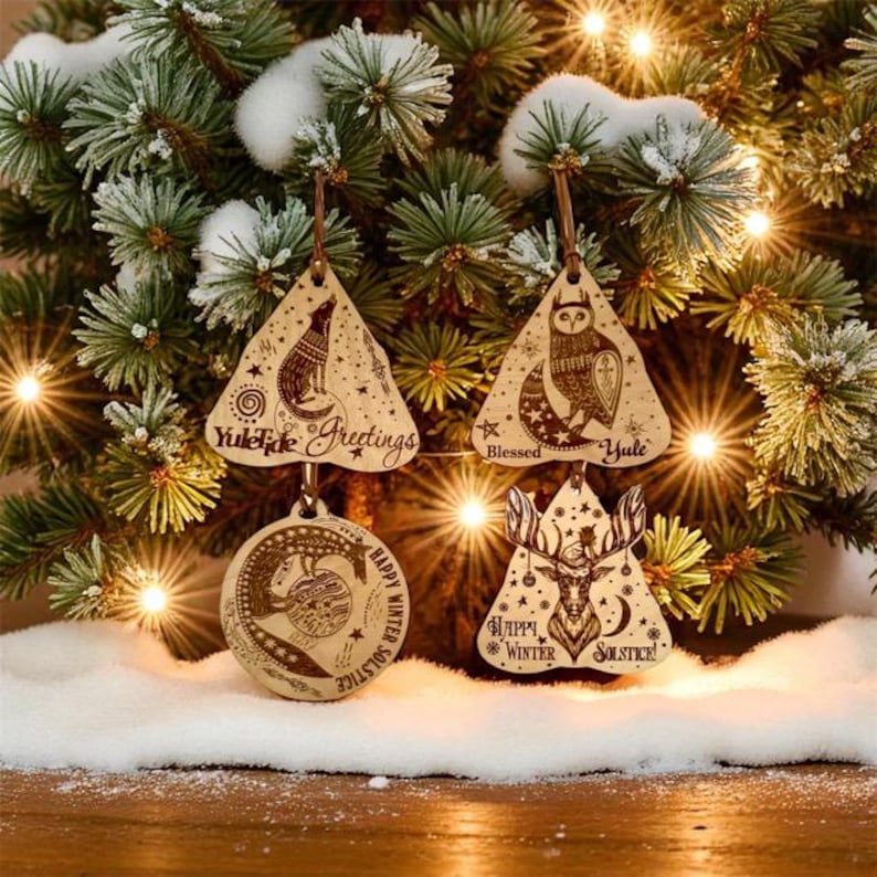 May include: Wooden Christmas ornaments hanging on a decorated tree. The ornaments are various shapes, including triangles and circles, and feature engraved designs of a wolf, owl, deer, and other winter-themed elements. Text includes "Yule Tide Greetings", "Blessed Yule", and "Happy Winter Solstice".