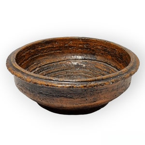 May include: A brown ceramic bowl with a textured, slightly rough surface. The bowl has a wide, rounded rim and a deep, slightly concave interior.