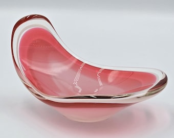 Könnte beinhalten: Eine klare Glasschale mit rosa Innenraum und einer geschwungenen, asymmetrischen Form. Die Schale hat eine glatte, glänzende Oberfläche und einen klaren Rand. Die rosa Farbe verblasst von einem dunkleren Farbton oben zu einem helleren Farbton unten.