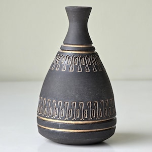 Könnte beinhalten: Eine schwarze Keramikvase mit geometrischem Muster in Gold. Die Vase hat einen breiten Boden und einen schmalen Hals.