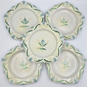 May include: Five off-white ceramic plates with a scalloped edge. Each plate features a central floral design in blue and green, with matching green and blue accents around the rim. The plates have a crackle finish.